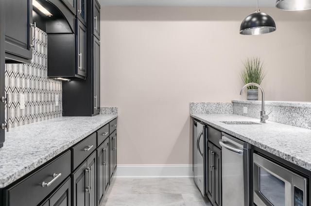 kitchen featuring dark cabinetry, a sink, decorative light fixtures, and light stone countertops