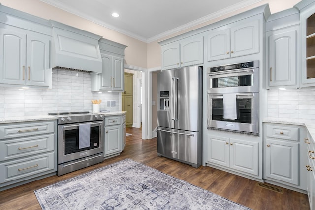 kitchen featuring glass insert cabinets, ornamental molding, light stone countertops, custom exhaust hood, and stainless steel appliances