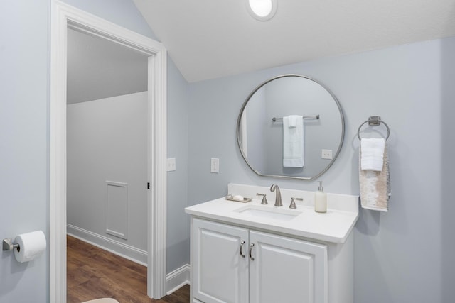 bathroom with baseboards, vaulted ceiling, wood finished floors, and vanity