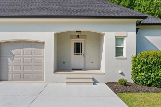 property entrance featuring a shingled roof, concrete driveway, an attached garage, and stucco siding