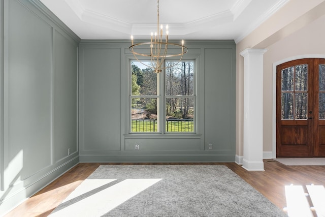 unfurnished dining area featuring ornate columns, a chandelier, a decorative wall, and a raised ceiling