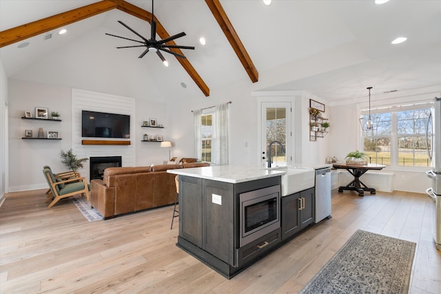 kitchen with a fireplace, stainless steel appliances, hanging light fixtures, a kitchen island with sink, and a sink