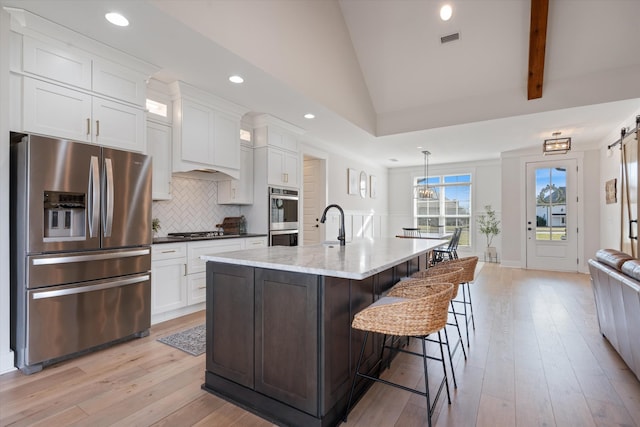 kitchen featuring a center island with sink, stainless steel appliances, tasteful backsplash, visible vents, and white cabinetry