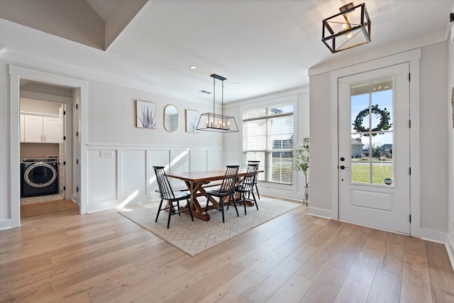 dining space featuring light wood finished floors, washer / clothes dryer, wainscoting, and a decorative wall