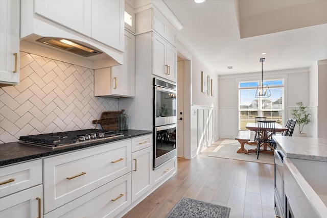 kitchen with decorative light fixtures, dark countertops, appliances with stainless steel finishes, light wood-style floors, and white cabinets