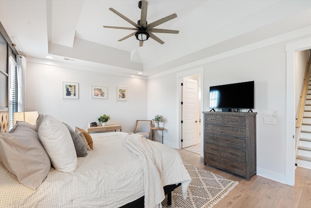 bedroom with a tray ceiling, visible vents, a ceiling fan, light wood-type flooring, and baseboards