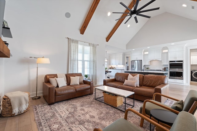 living area featuring beam ceiling, light wood finished floors, washer / clothes dryer, ceiling fan, and high vaulted ceiling