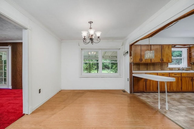 unfurnished dining area featuring a chandelier, crown molding, light wood-style flooring, and a sink