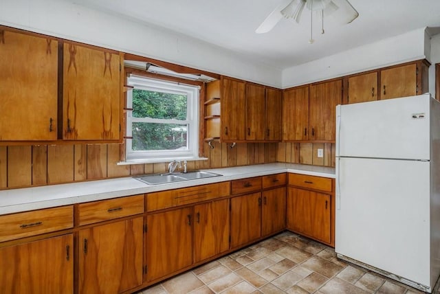 kitchen with brown cabinets, freestanding refrigerator, light countertops, and a sink