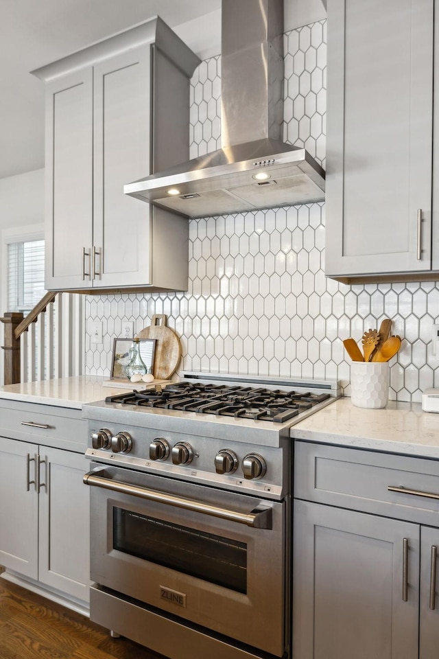 kitchen with wall chimney exhaust hood, stainless steel range, backsplash, and gray cabinetry