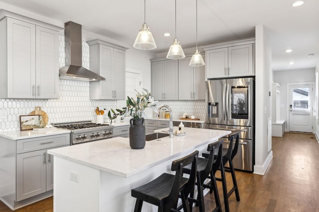 kitchen with wall chimney range hood, stainless steel refrigerator with ice dispenser, gray cabinets, light stone countertops, and dark wood finished floors