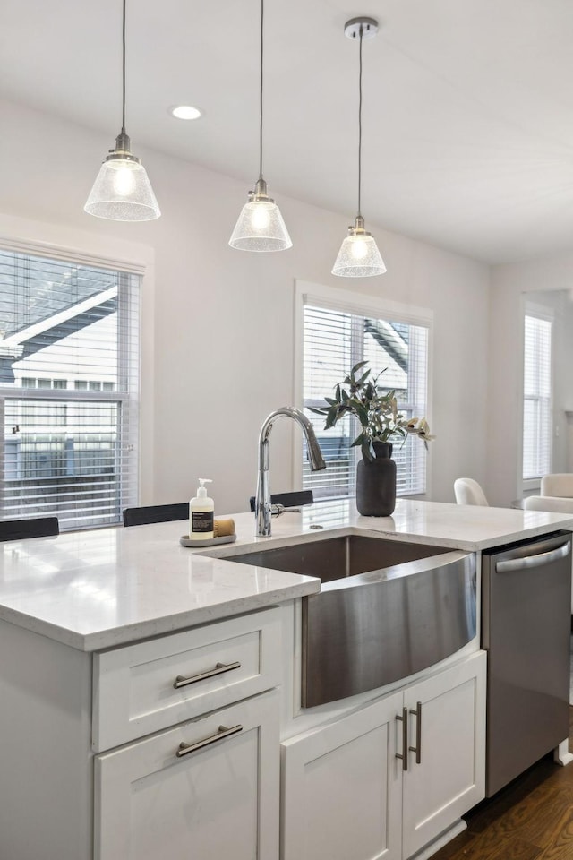 kitchen featuring dark wood-style flooring, pendant lighting, stainless steel dishwasher, white cabinetry, and a sink