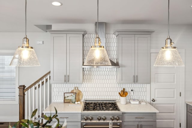 kitchen featuring stainless steel stove, wall chimney range hood, gray cabinets, decorative backsplash, and pendant lighting