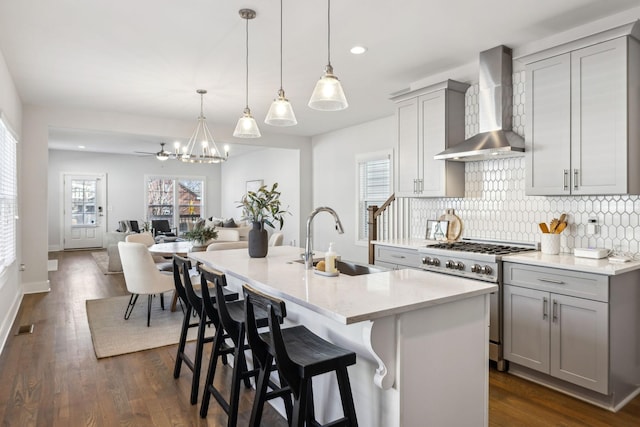 kitchen featuring high end stainless steel range, gray cabinets, decorative backsplash, a sink, and wall chimney range hood