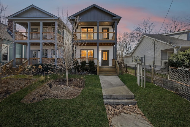 view of front of property with covered porch, board and batten siding, fence, a balcony, and a front lawn