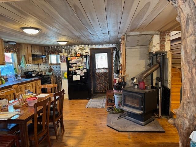 kitchen featuring wood ceiling, ventilation hood, light wood-type flooring, black appliances, and a wood stove