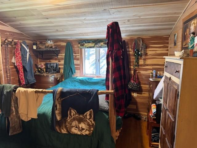 bedroom featuring vaulted ceiling, wooden ceiling, wood walls, and wood finished floors