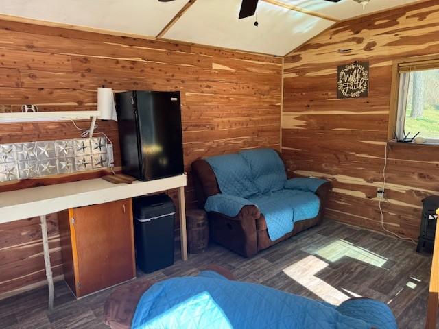 living area with wood walls, ceiling fan, and vaulted ceiling