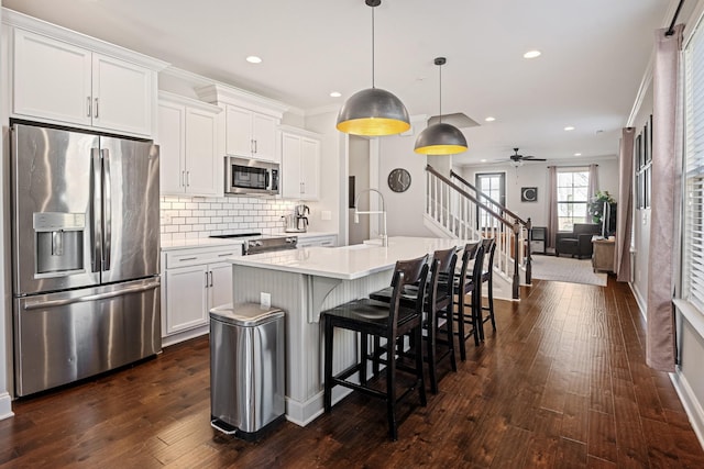 kitchen with light countertops, hanging light fixtures, appliances with stainless steel finishes, a kitchen island with sink, and white cabinets