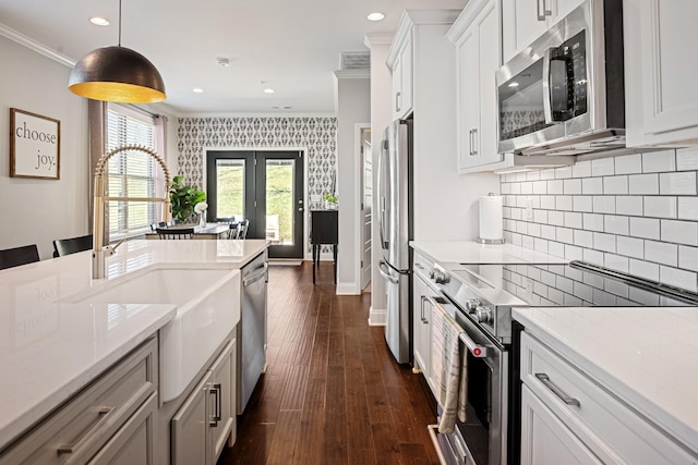 kitchen with ornamental molding, appliances with stainless steel finishes, white cabinetry, and decorative light fixtures