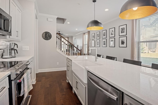 kitchen with appliances with stainless steel finishes, decorative light fixtures, light stone countertops, crown molding, and white cabinetry