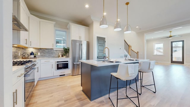 kitchen with light countertops, appliances with stainless steel finishes, a center island with sink, and white cabinetry