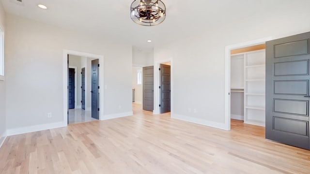 unfurnished bedroom with a walk in closet, baseboards, light wood finished floors, and recessed lighting