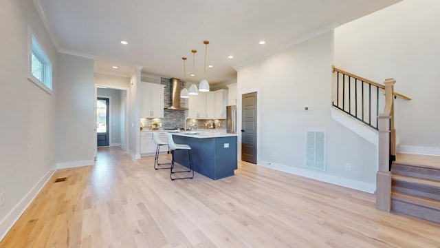 kitchen featuring a center island, decorative light fixtures, light countertops, white cabinetry, and wall chimney exhaust hood