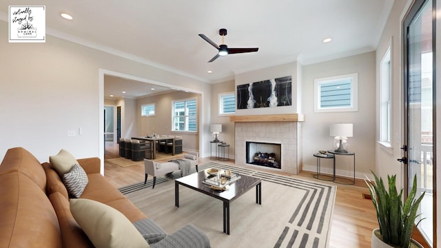 living area with ornamental molding, a tiled fireplace, light wood-style flooring, and baseboards