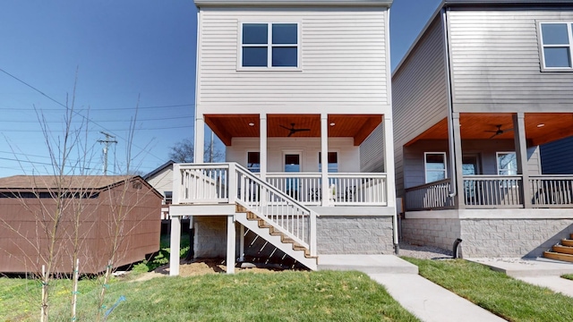 view of front of home with covered porch, ceiling fan, stairway, and a front yard