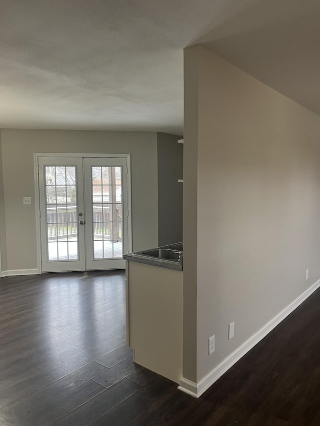 empty room featuring dark wood-type flooring, french doors, and baseboards