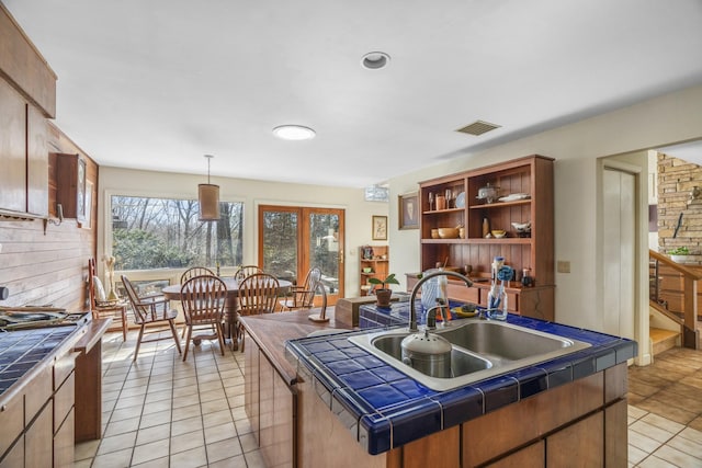 kitchen with a center island with sink, visible vents, tile counters, open shelves, and a sink