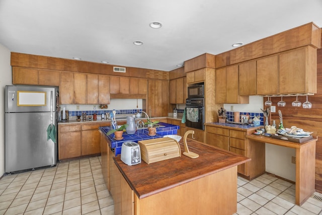 kitchen with black appliances, an island with sink, visible vents, and brown cabinets