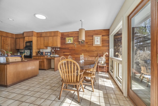 kitchen featuring brown cabinets, light tile patterned floors, hanging light fixtures, wood walls, and black appliances