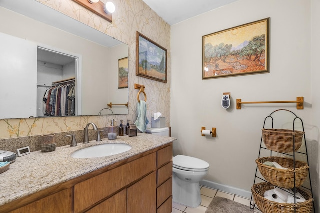 bathroom featuring tile patterned flooring, toilet, vanity, baseboards, and a walk in closet