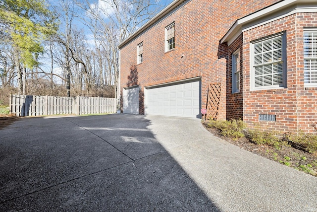 view of side of property featuring concrete driveway, crawl space, an attached garage, fence, and brick siding