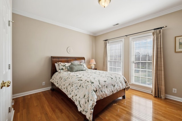 bedroom with ornamental molding, wood finished floors, visible vents, and baseboards