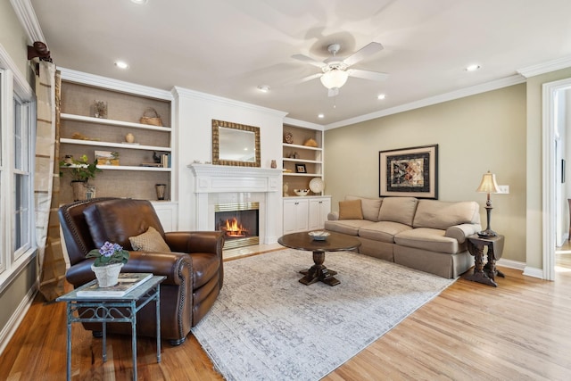 living room featuring baseboards, a lit fireplace, light wood-type flooring, and crown molding