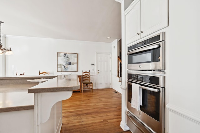 kitchen with pendant lighting, a warming drawer, light wood-style floors, stainless steel double oven, and white cabinetry