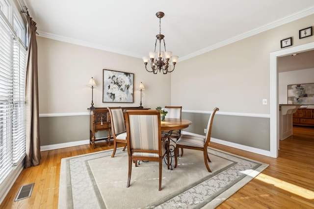 dining area featuring a chandelier, light wood-style flooring, visible vents, and crown molding