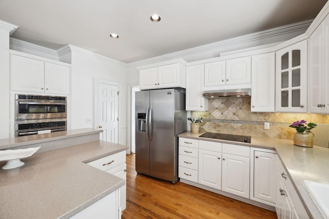 kitchen with under cabinet range hood, appliances with stainless steel finishes, glass insert cabinets, and white cabinetry