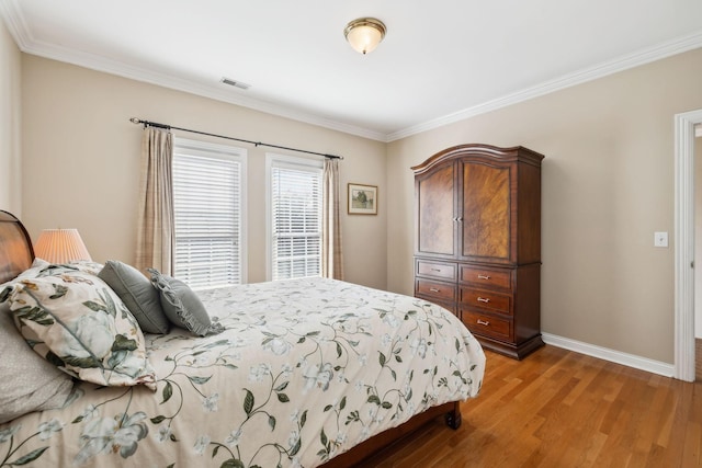 bedroom featuring light wood finished floors, baseboards, visible vents, and ornamental molding