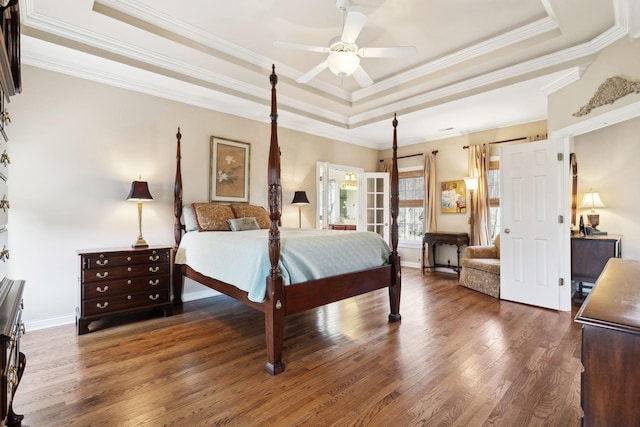 bedroom featuring dark wood-style floors, french doors, a raised ceiling, ornamental molding, and baseboards