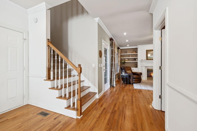 interior space featuring light wood finished floors, stairs, visible vents, and crown molding