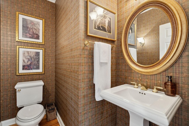 half bath with toilet, wallpapered walls, and a sink