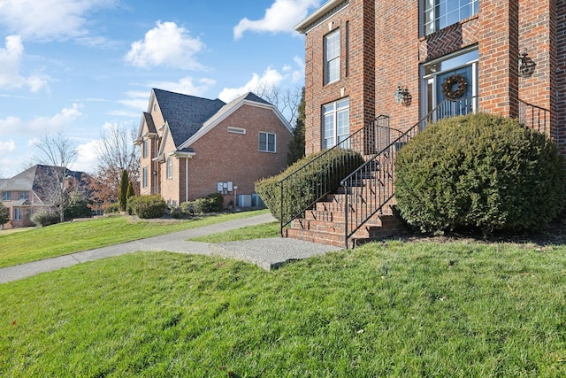 view of side of property featuring stairway, a lawn, and brick siding