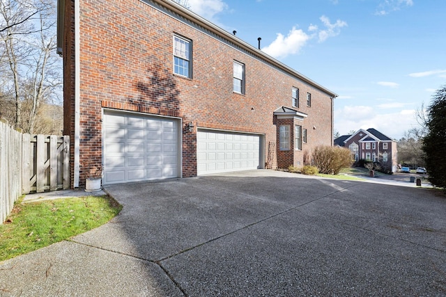 exterior space featuring a garage, concrete driveway, brick siding, and fence