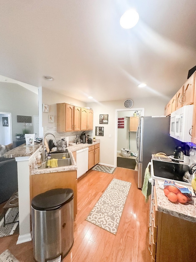 kitchen featuring white appliances, light wood-style flooring, a peninsula, light brown cabinetry, and a sink