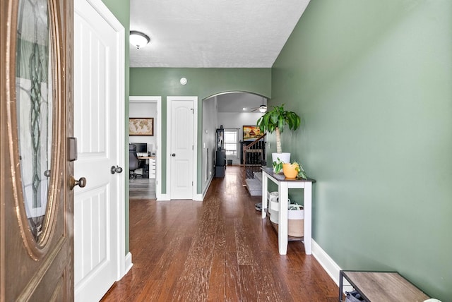 corridor with baseboards, arched walkways, stairway, wood finished floors, and a textured ceiling