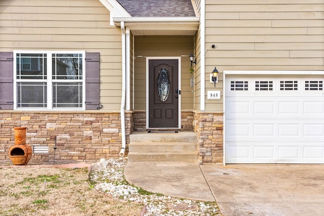 property entrance featuring a shingled roof, stone siding, a garage, and concrete driveway